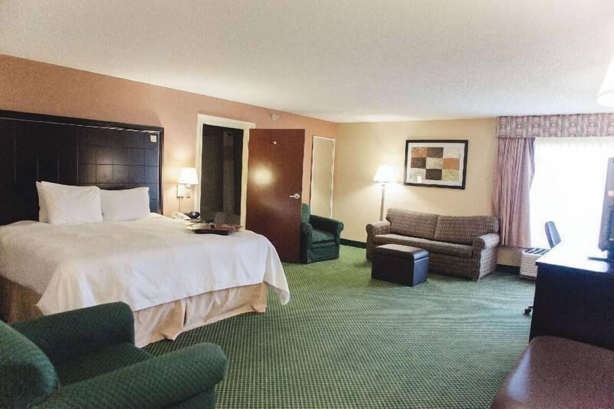 A hotel room with a large bed, a desk, a chair, a sofa, and a small table.