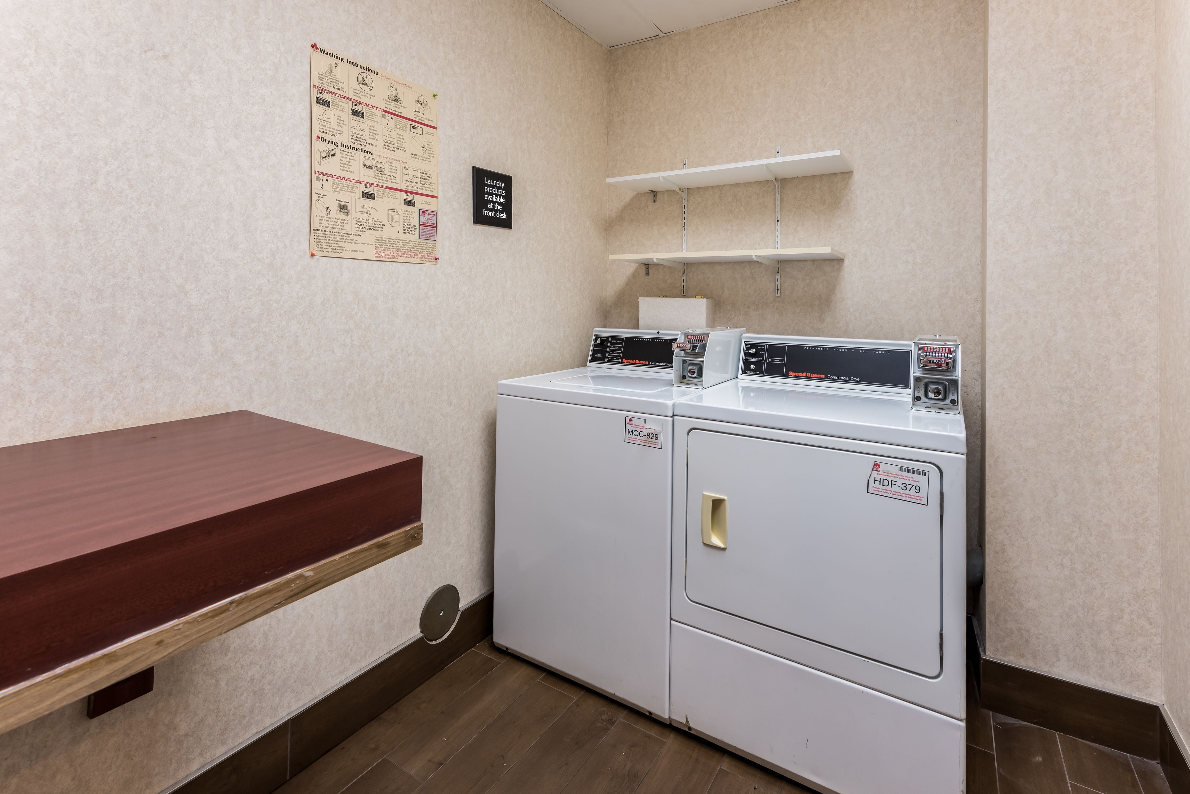 A laundry room with two white washers and dryers, a wooden bench, and a bulletin board with laundry instructions.