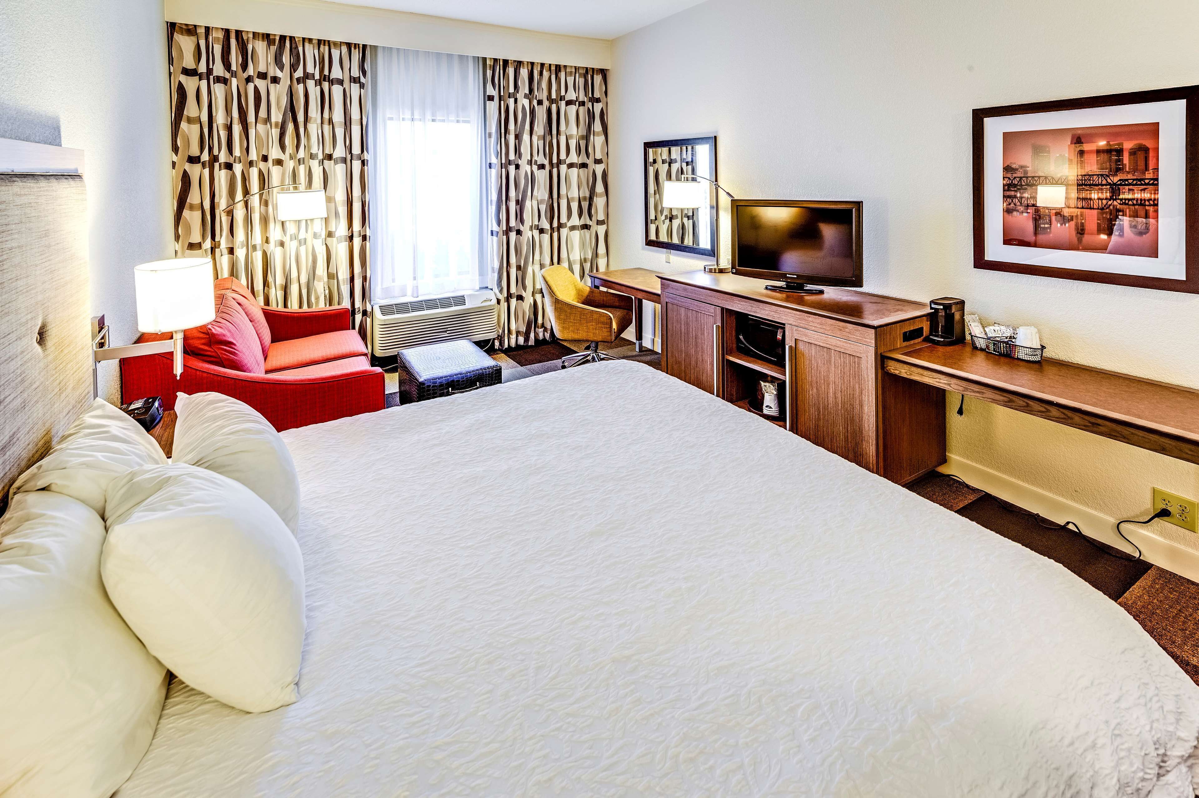 Une chambre d’hôtel avec un grand lit, un bureau avec un ordinateur, une chaise, une télévision et un tableau encadré au mur.