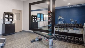 A gym with a bench, dumbbells, and a mirror reflecting the room.