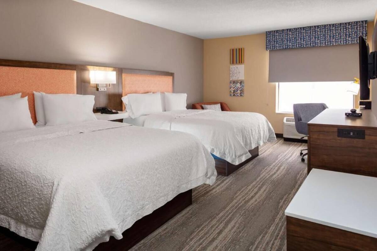 Une chambre d’hôtel avec deux lits, un bureau, une chaise, une télévision et une fenêtre.