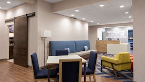A hotel lobby with a reception desk, a seating area with a sofa and chairs, and a dining table with chairs.