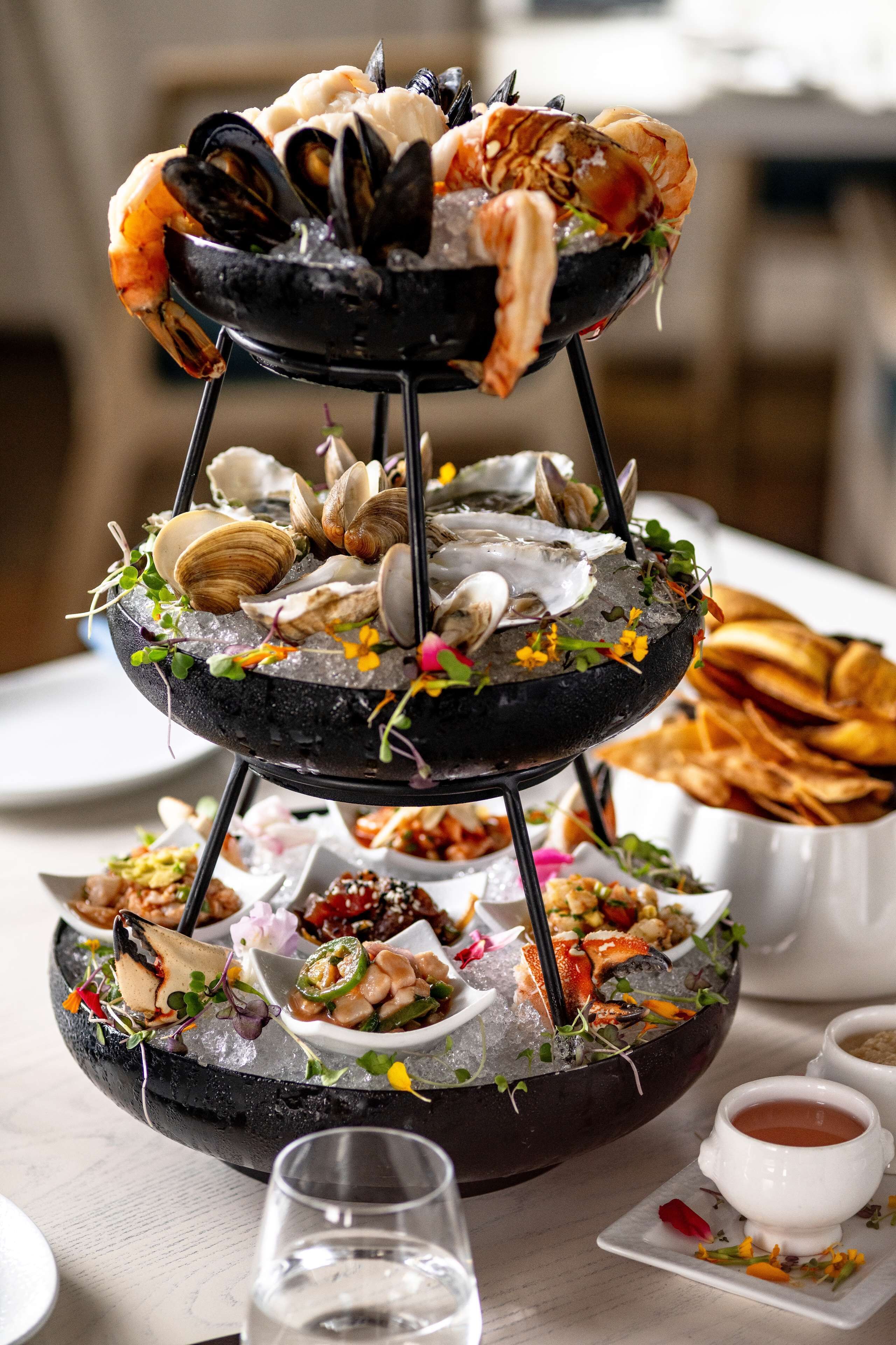 Un plateau de fruits de mer comprenant des palourdes, des moules et des crevettes, présenté sur un présentoir noir.