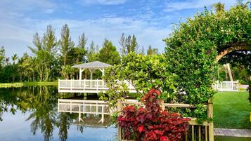 A serene lakeside garden with a gazebo, lush greenery, and a clear reflection in the water.