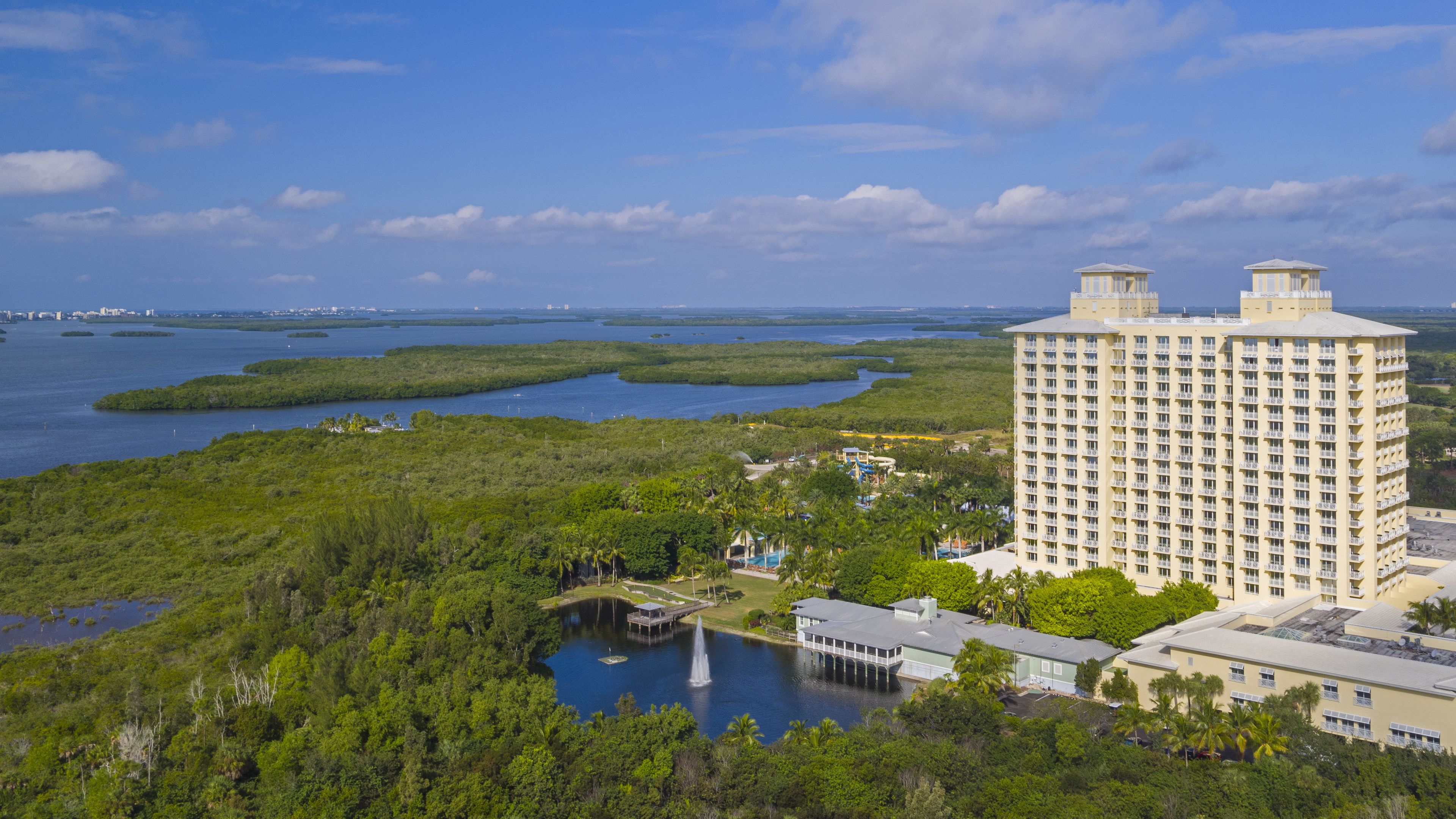 A high-rise hotel with a view of a mangrove forest and water bodies.