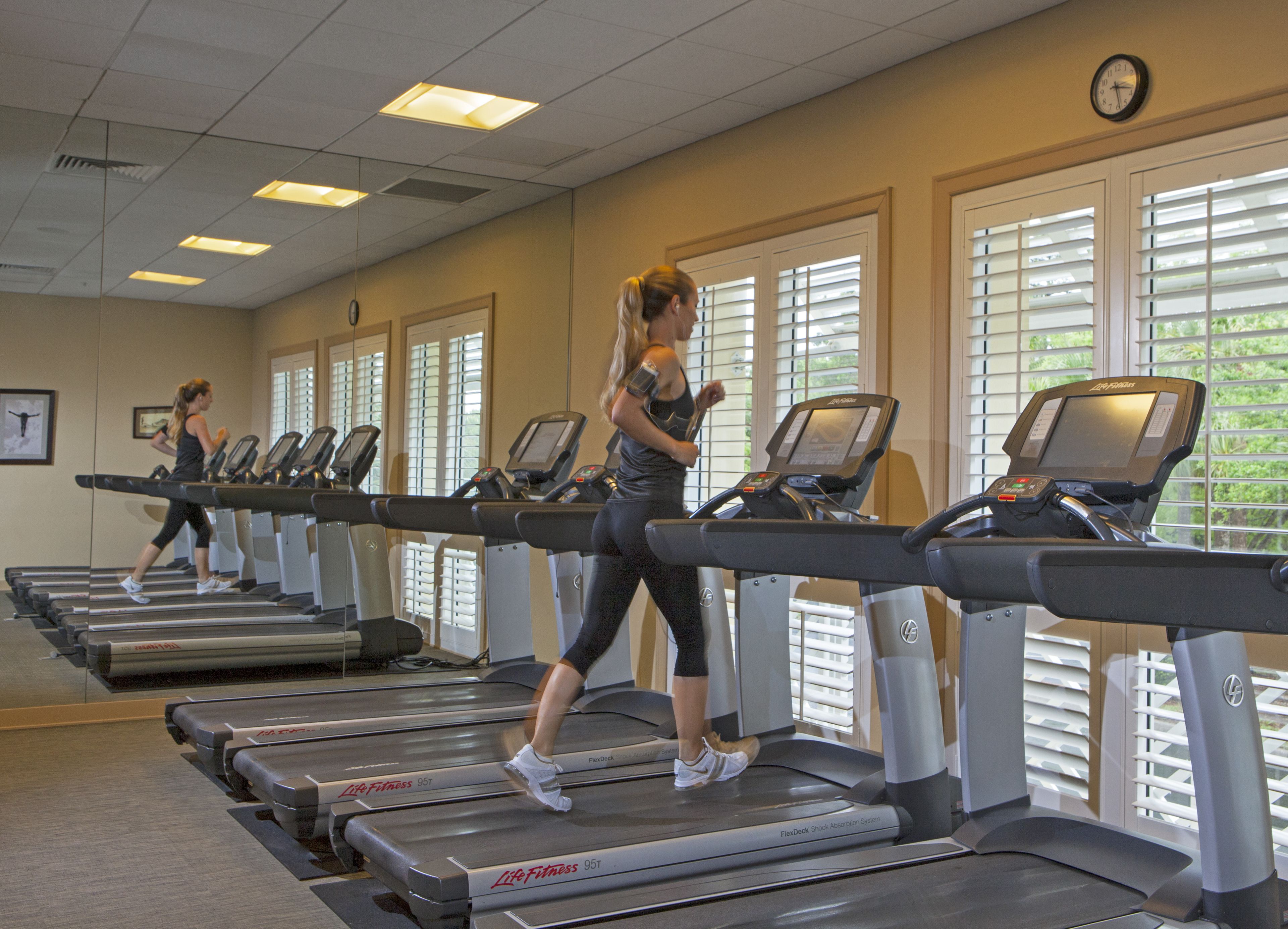 A gym with treadmills, mirrors, and windows with blinds.