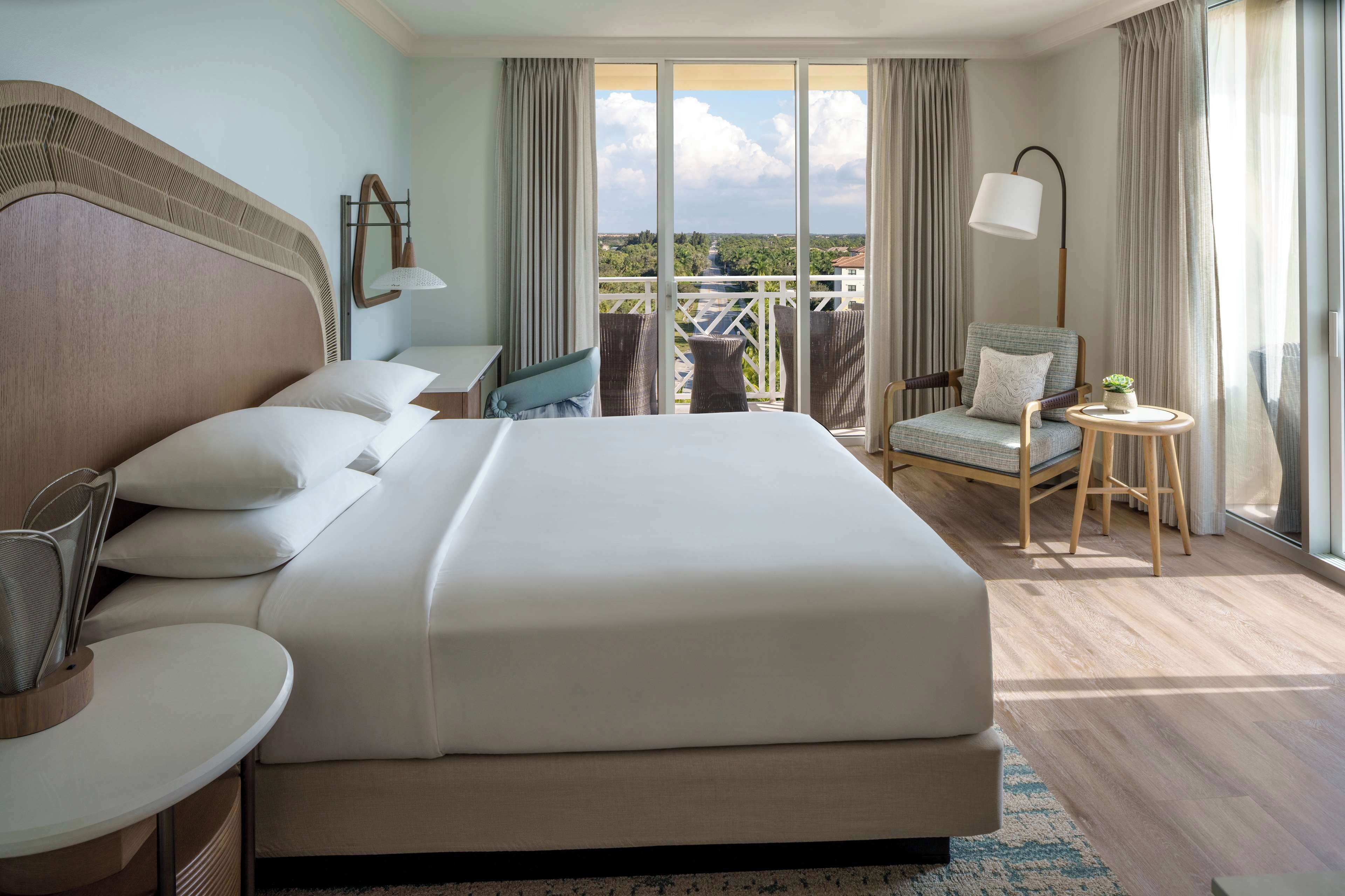 Ein Hotelzimmer mit einem großen Bett, einem Sessel, einem kleinen Tisch und Blick ins Freie.