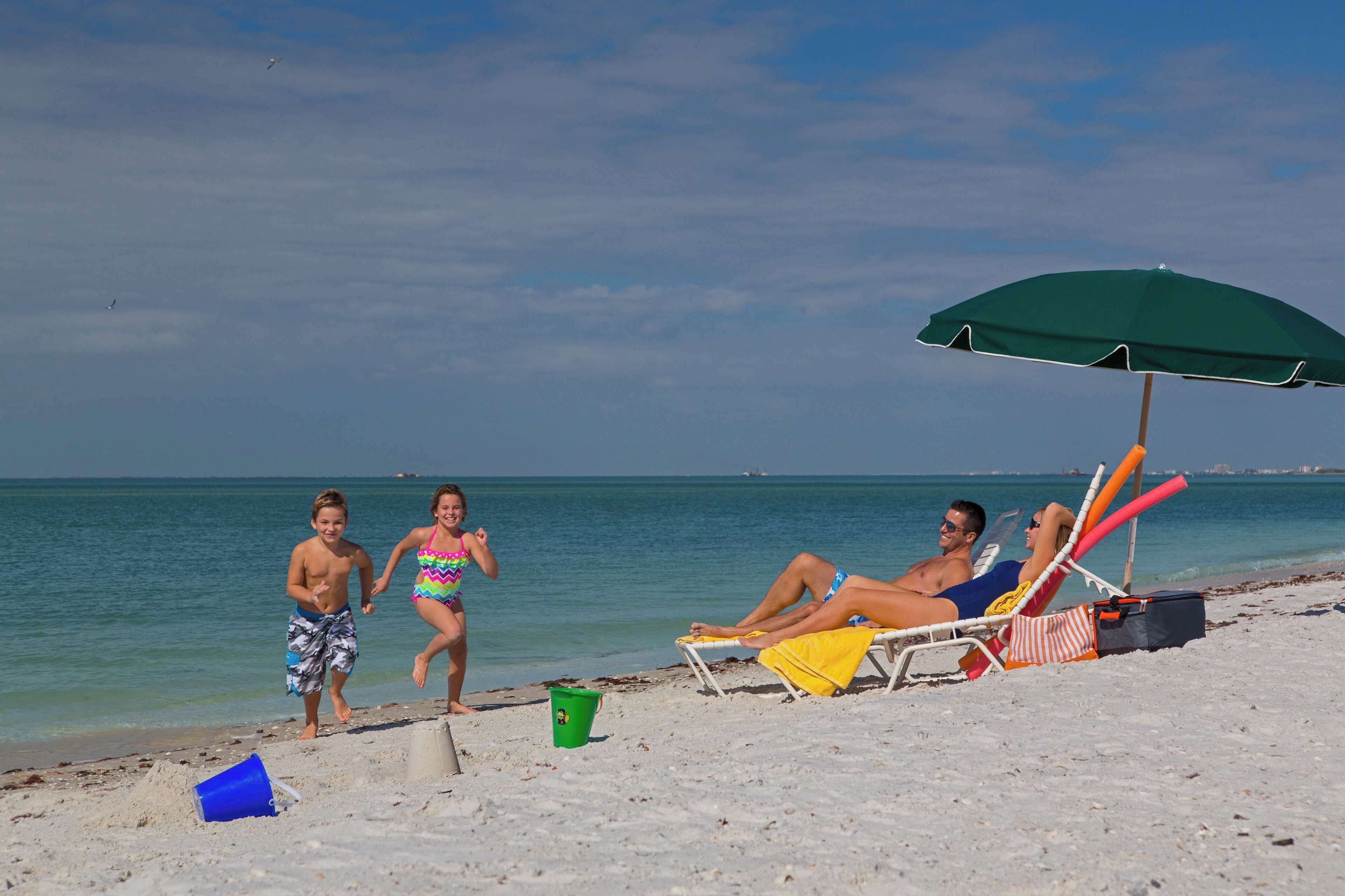 Een zandstrand met een groene parasol, een ligstoel en een emmer.