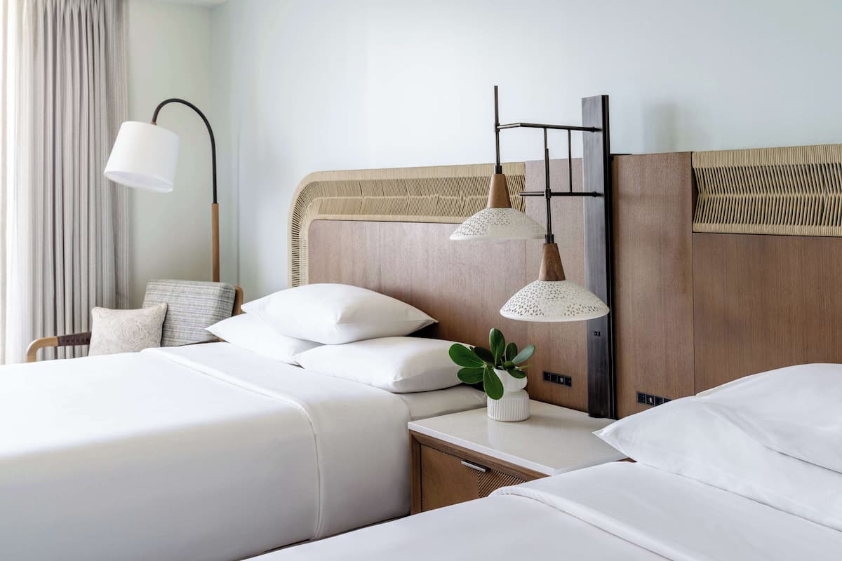 A hotel room with two beds, a nightstand, a lamp, and a plant.
