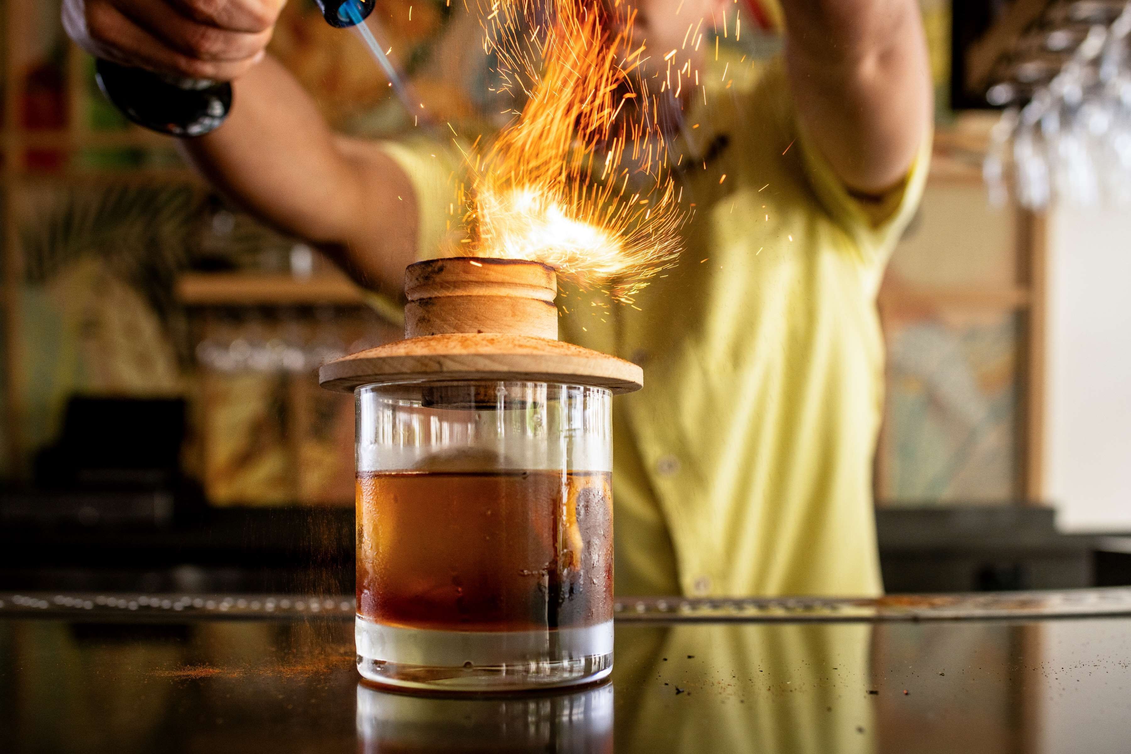 Eine Person benutzt einen Brenner auf einem Glasbehälter mit Holzlöffel, wobei Funken fliegen.