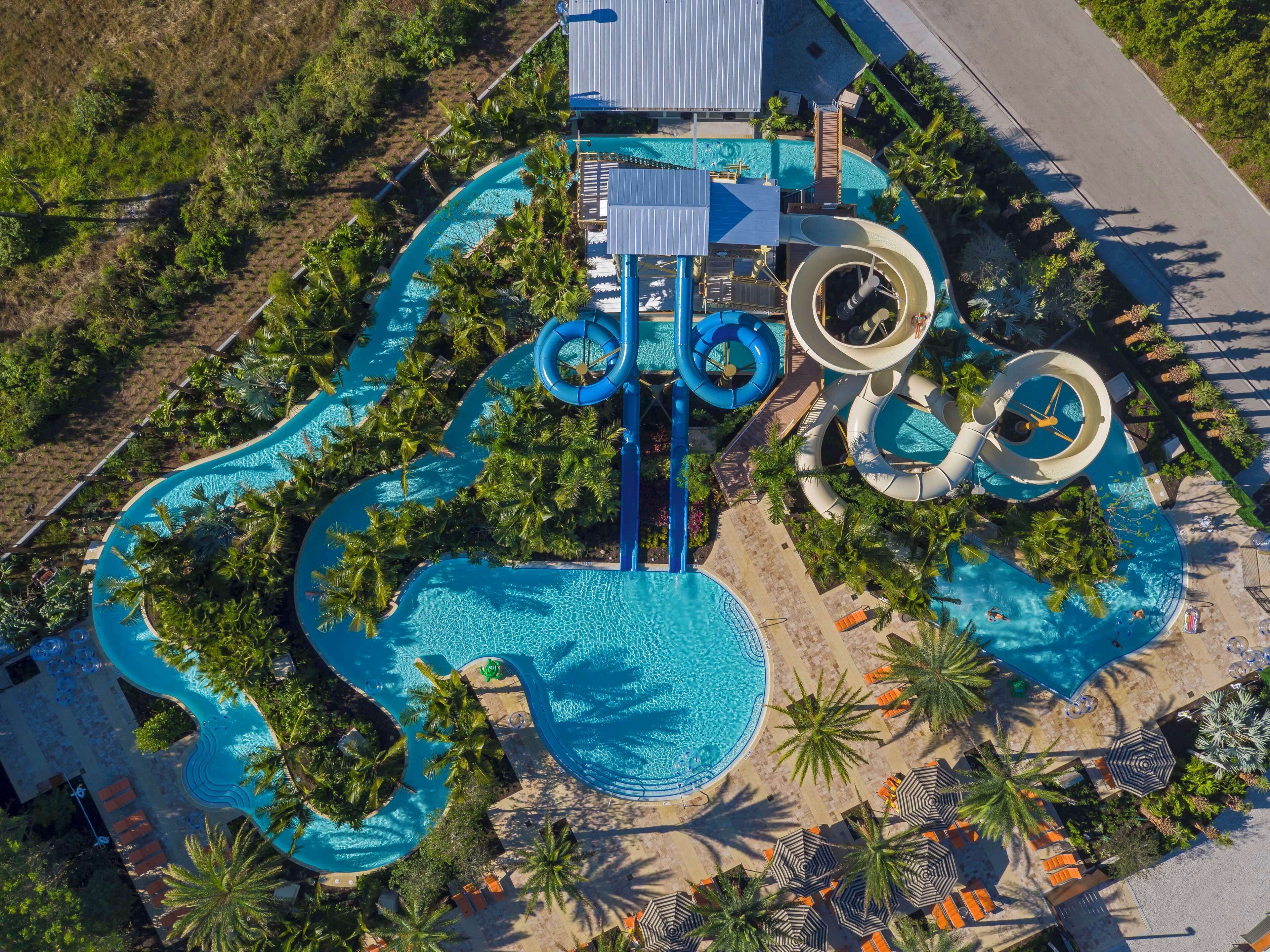 An aerial view of a resort with multiple swimming pools, water slides, and palm trees.
