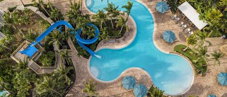 A large pool with a winding design, surrounded by palm trees and lounge areas with umbrellas.