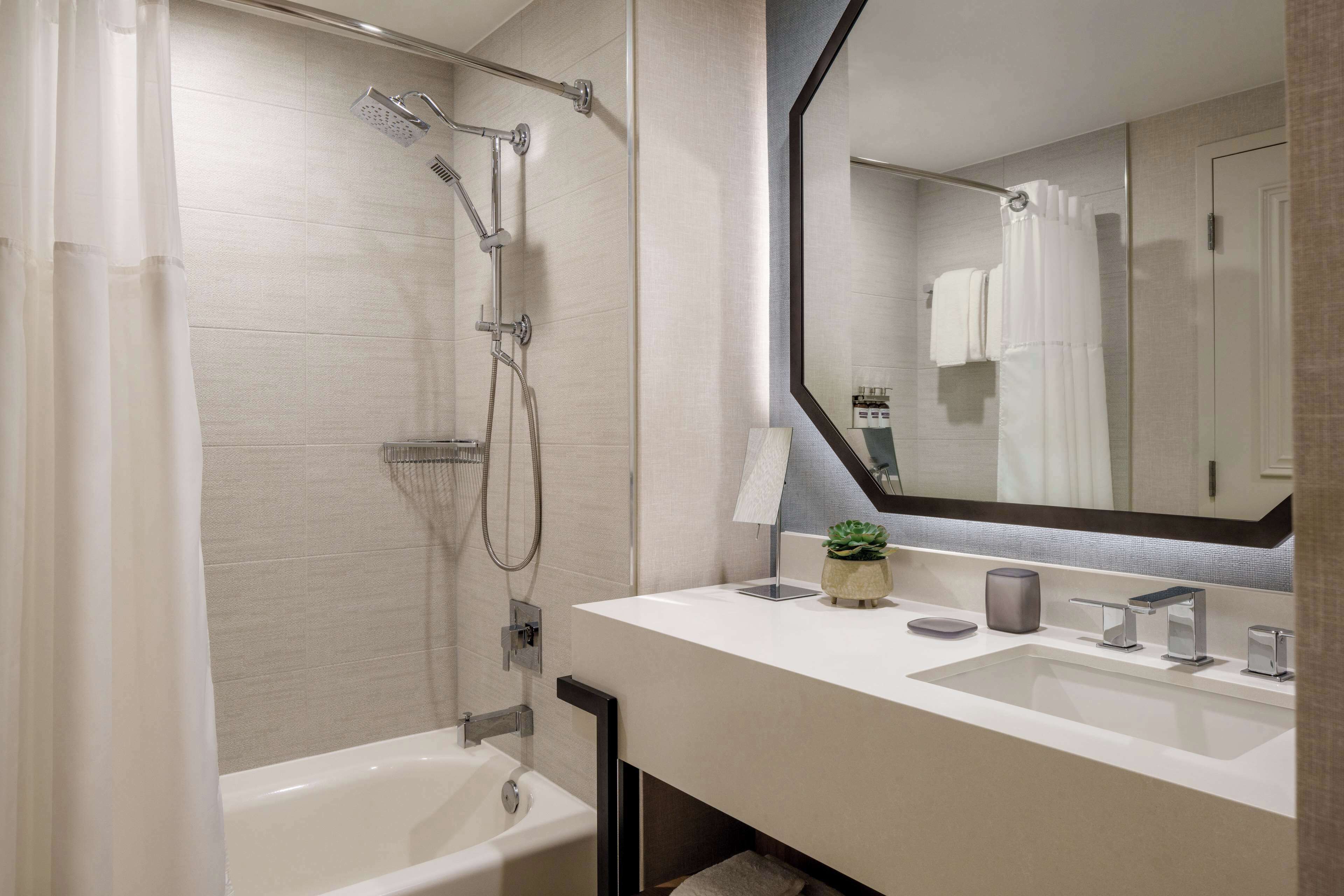 A modern bathroom with a bathtub, a shower with a rain showerhead, and a large mirror above the sink.