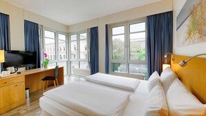 A hotel room with a bed, desk, chair, television, and large windows. - Hotel Berlin Mitte by Coffee Fellows (Berlin)