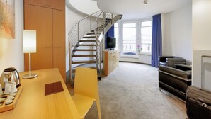 A modern hotel room with a wooden desk, a yellow chair, a spiral staircase, a television, and a large window with curtains. - Hotel Berlin Mitte by Coffee Fellows (Berlin)