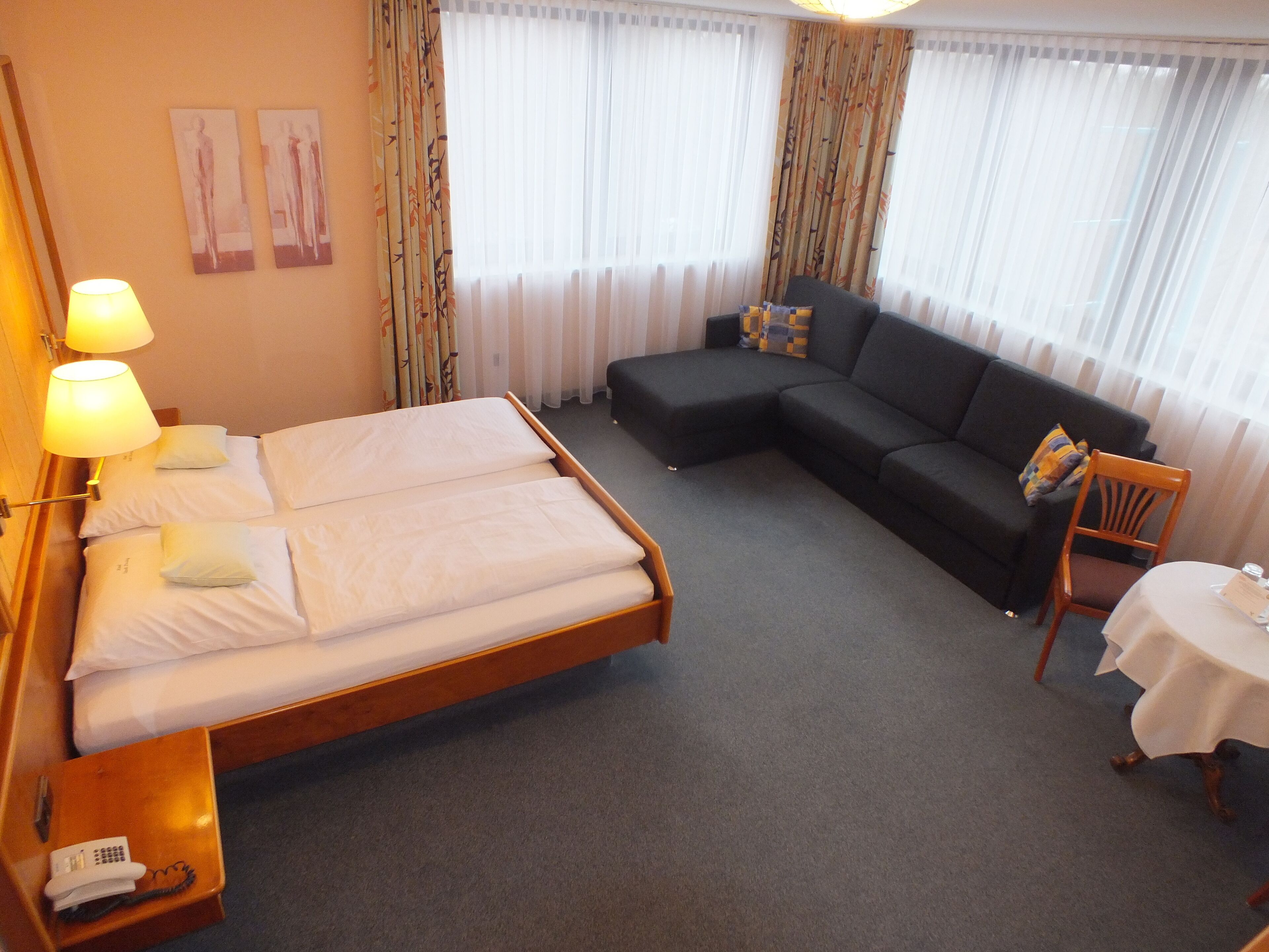 A hotel room with a double bed, a sofa, a small table with a chair, and a telephone on a side table.