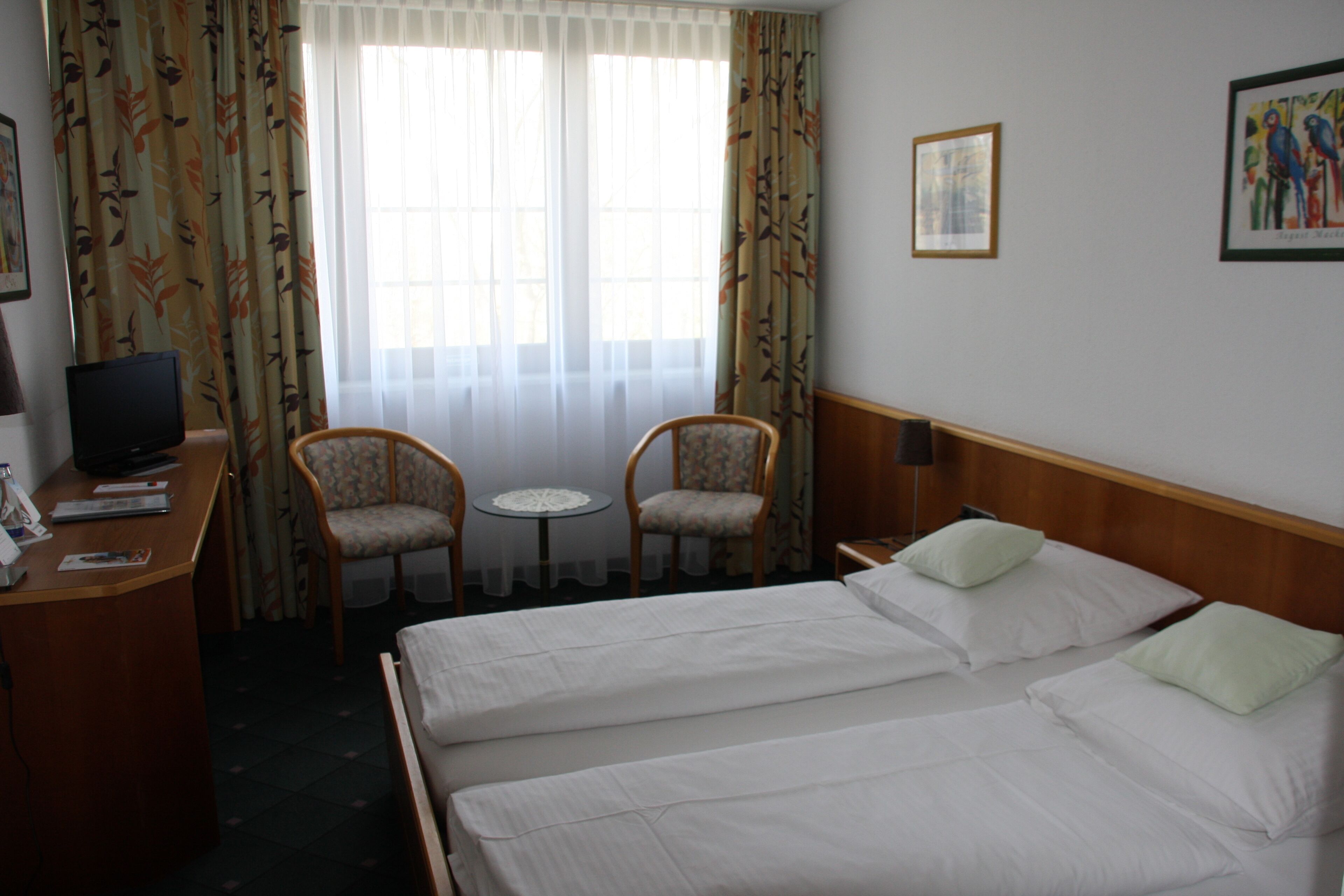Habitación de hotel con dos camas, un escritorio con televisor, dos sillas y una mesita.