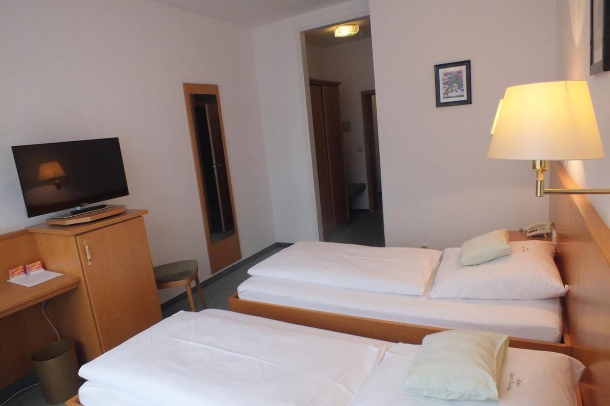 Et hotelværelse med to enkeltsenge, et skrivebord med fjernsyn, lampe og telefon.