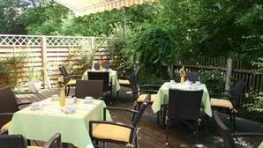 An outdoor patio with tables and chairs, surrounded by greenery and a wooden fence. - Hotel Stadt Pasing (Munich)