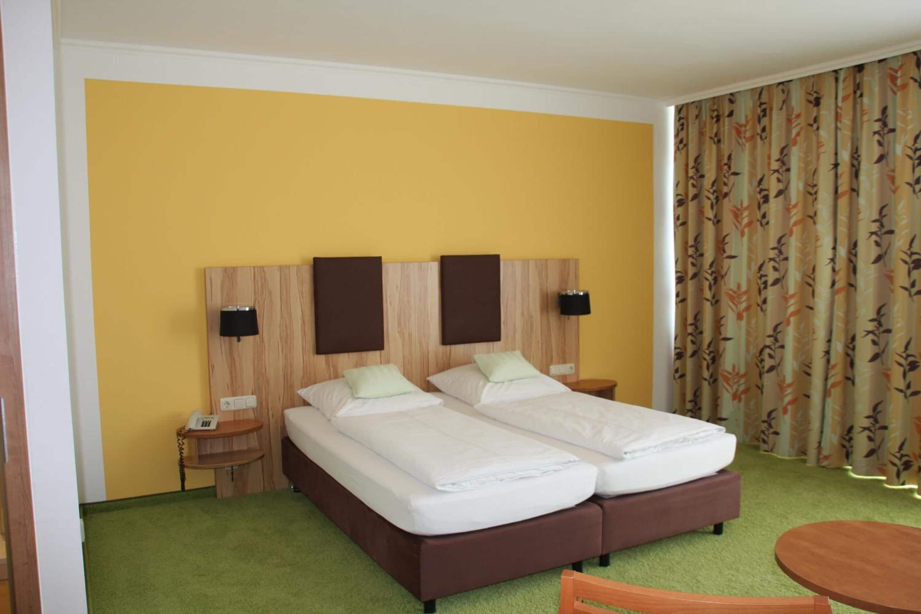 A double bed with a wooden headboard, two bedside tables, a small table, and a green carpet.