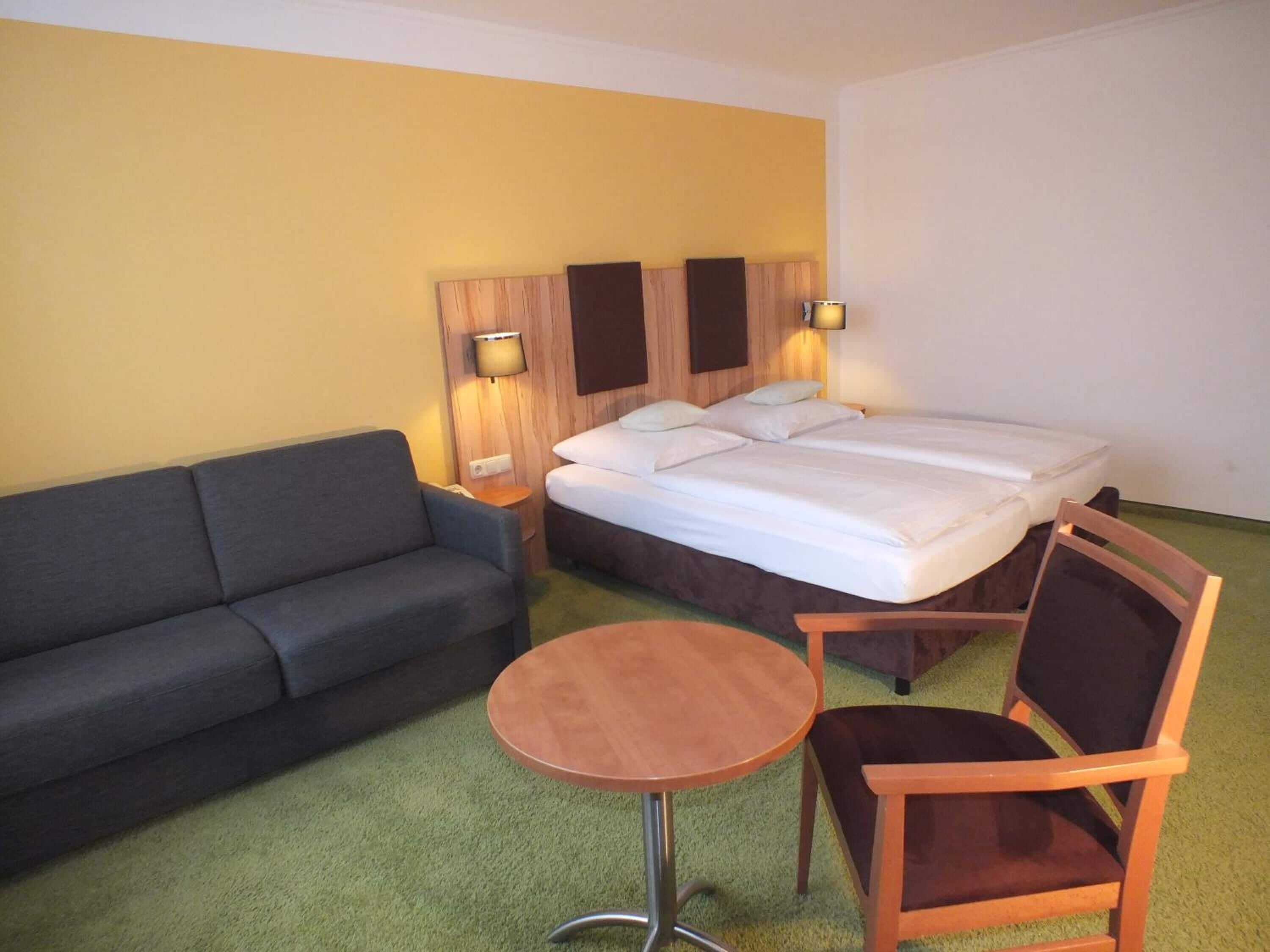 A hotel room with a bed, a sofa, a small round table, and two lamps.