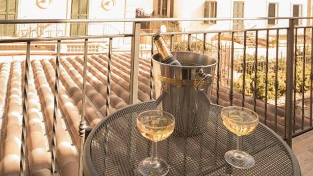 A rooftop terrace with a round metal table, two glasses of wine, and a bottle of champagne. - Hotel Donatello (Rome)