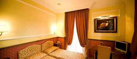 A hotel room with two beds, a desk, a television, and a painting on the wall.