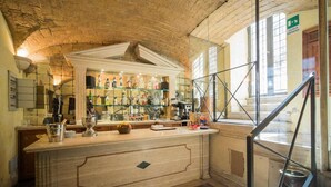 A bar area with a marble countertop, shelves with bottles, and a staircase with a glass railing. - Hotel Donatello (Rome)