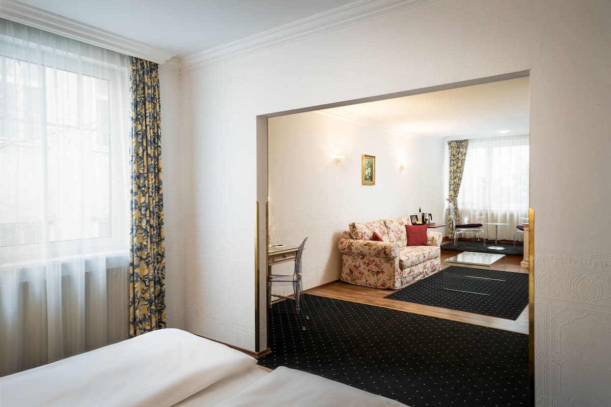 A hotel room with a bed, a desk, a sofa, and a view of the street.