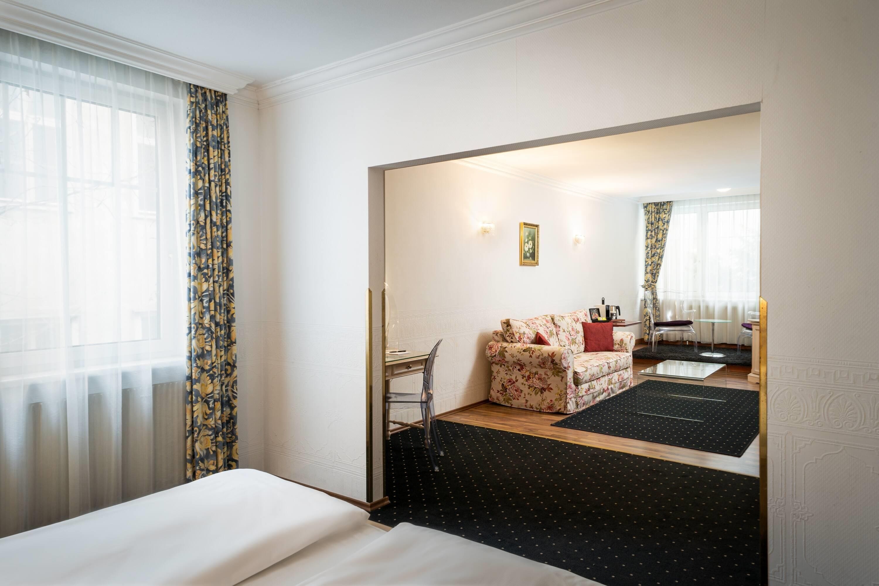A hotel room with a bed, a desk, a sofa, and a dining area.