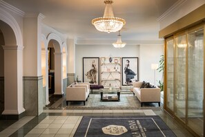 Um hall de hotel com um lustre, sofás, uma mesa de centro e obras de arte emolduradas.