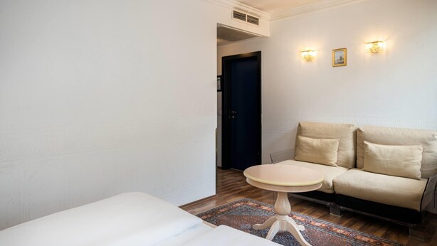 A hotel room with a bed, a small round table, a sofa, and a patterned rug. - Arthotel ANA Gala, Trademark Collection by Wyndham (Vienna)