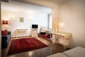 A modern living room with a sofa, a small table, a TV, and a desk with a chair. - Arthotel ANA Gala, Trademark Collection by Wyndham (Vienna)
