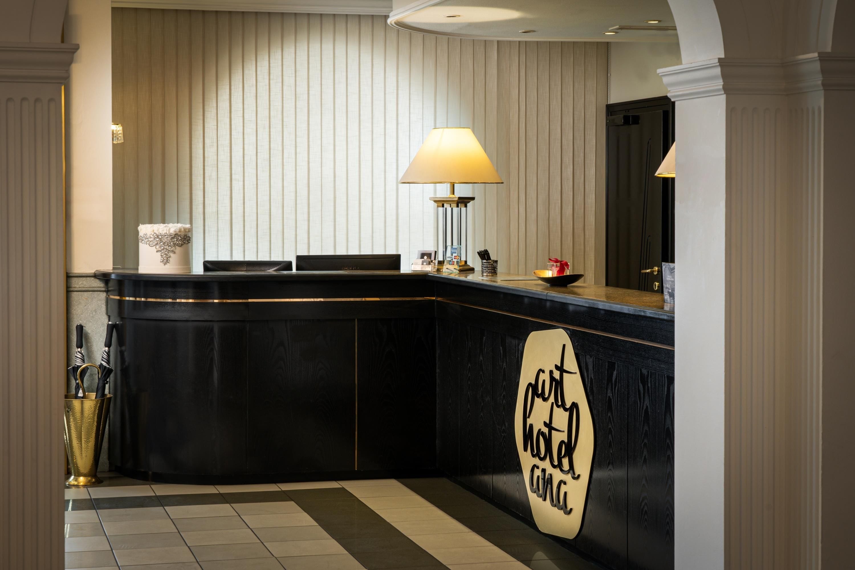 A hotel reception desk with a black counter, a lamp, and a sign that reads 'part of the hotel chain.'