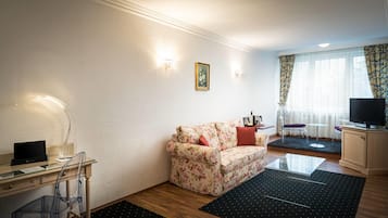 Ein modernes Wohnzimmer mit einem floralen Sofa, einem Glastisch, einem Flachbildfernseher und einem Schreibtisch mit einem Computer.