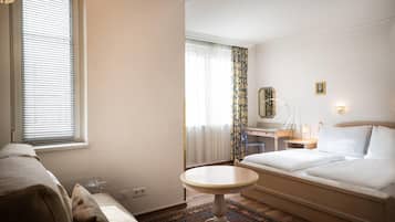 Ein Hotelzimmer mit Bett, Schreibtisch, Stuhl, rundem Tisch und einem Fenster mit Jalousien.