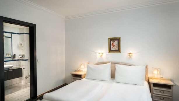 A hotel room with a bed, bedside tables, a nightstand, a mirror, and a framed picture on the wall. - Arthotel ANA Gala, Trademark Collection by Wyndham (Vienna)