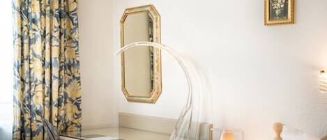 A hotel room with a glass desk, a mirror, a lamp, and a framed picture on the wall.
