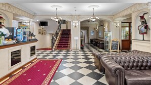 Eine Hotelhalle mit Schachbrettmuster-Boden, einem roten Teppich, einer Treppe und einer Bar.