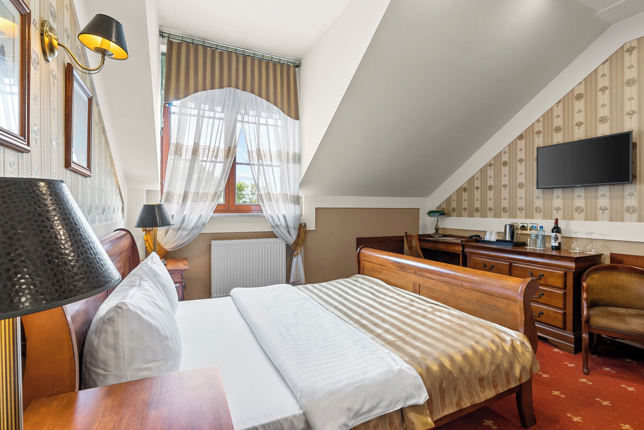 A hotel room with a bed, a desk, a chair, a television, and a window with curtains.