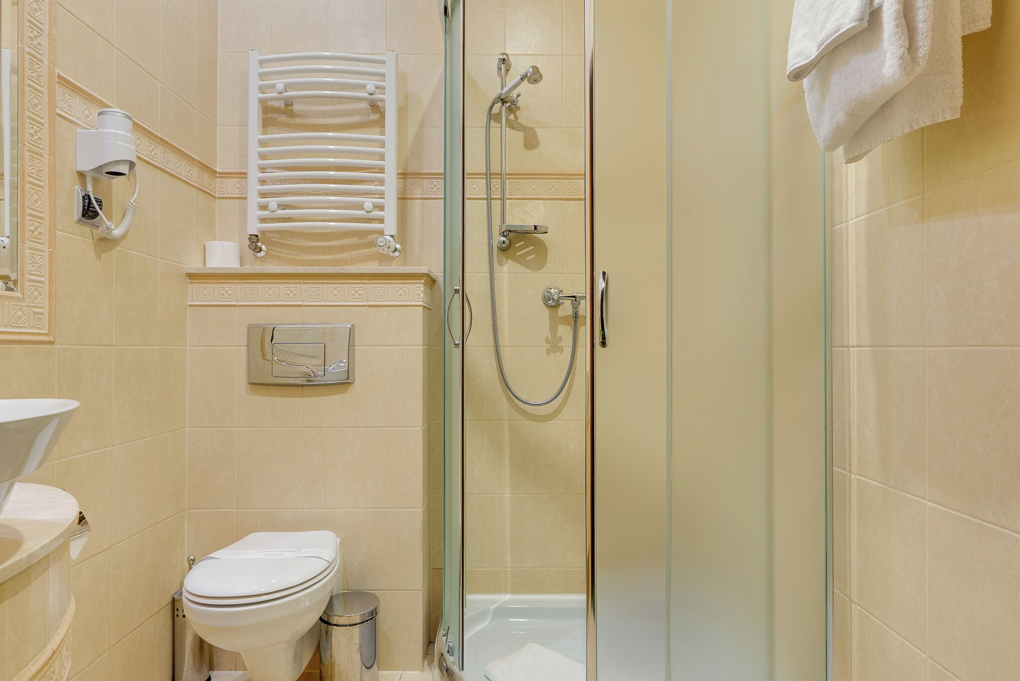 Un baño con inodoro, bidé, ducha con mampara de vidrio y un perchero para toallas.