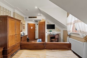 A bedroom with a bed, wooden wardrobe, desk, chair, and a television.