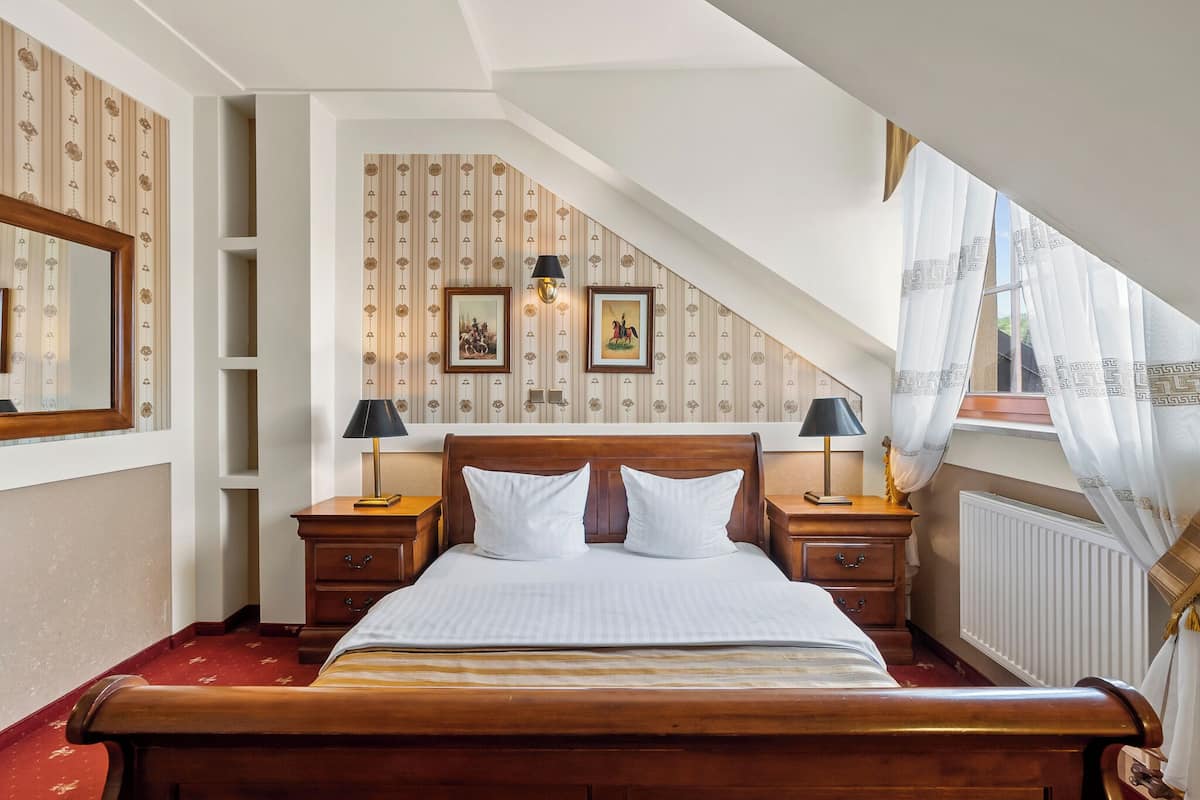 A bedroom with a wooden bed, two bedside tables with lamps, a large mirror, and a sloped ceiling.