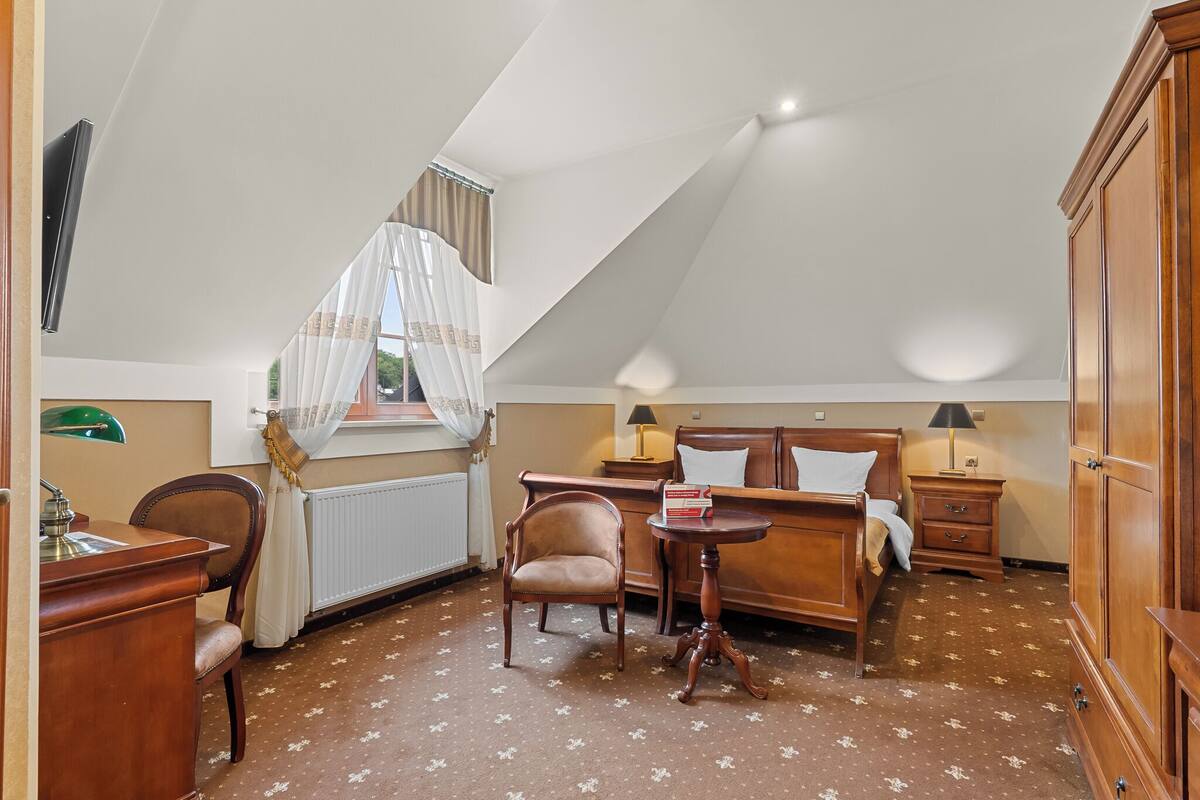 A room with a bed, a desk, a chair, a small table, and a wardrobe.
