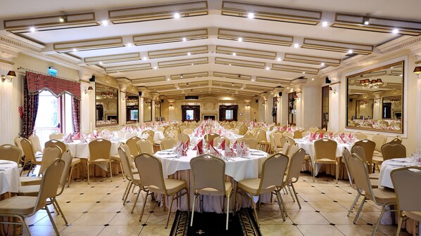 A banquet hall with round tables set for a formal event, featuring chandeliers and a large mirror on the wall.