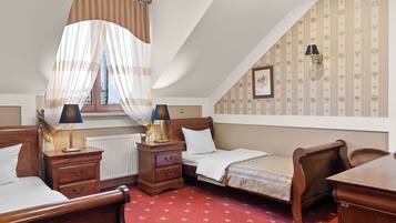 A bedroom with a bed, two bedside tables with lamps, a chair, a desk, a radiator, and a window with curtains.