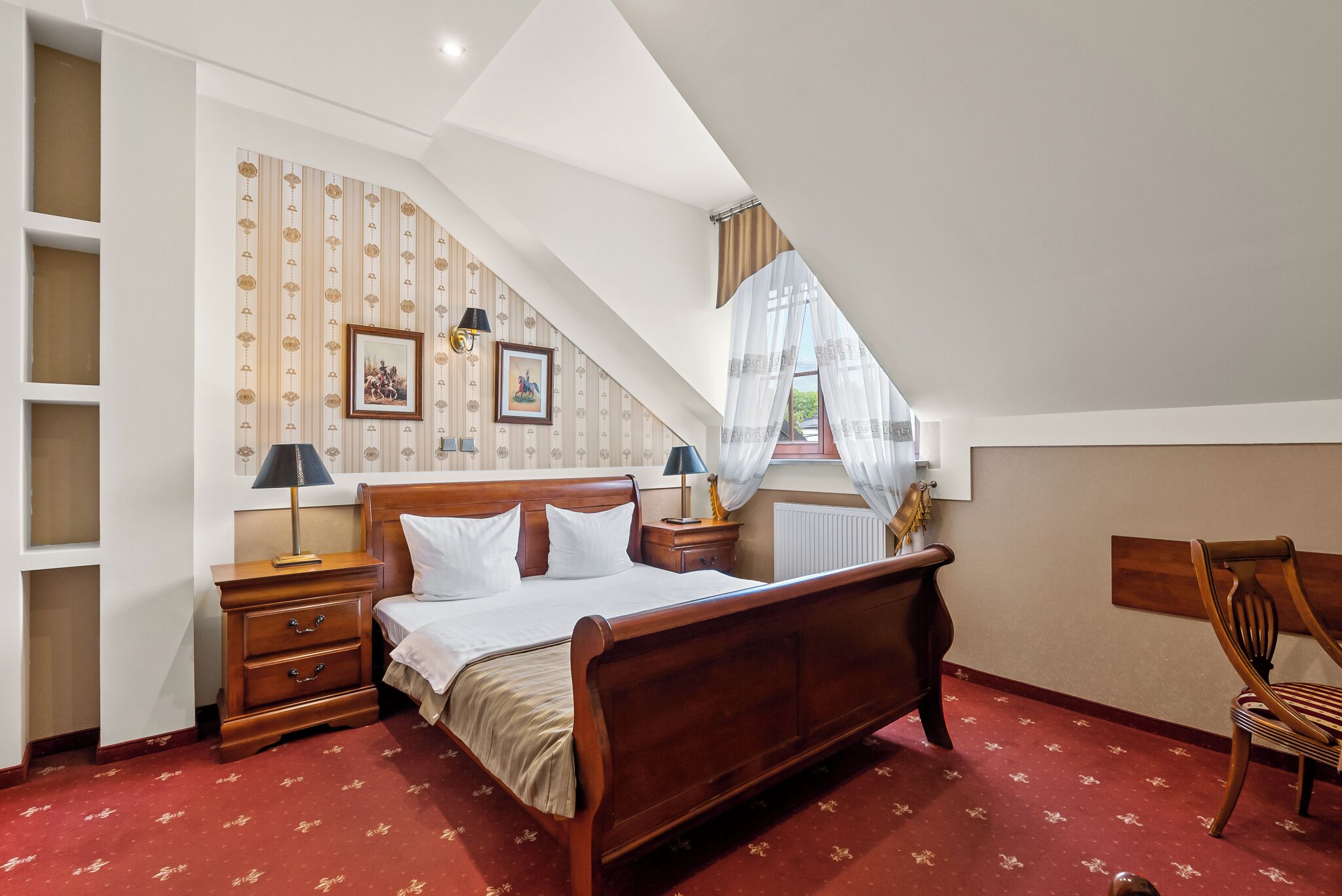 A bedroom with a wooden bed, nightstands, a chair, and a window with sheer curtains.