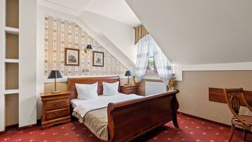 A bedroom with a wooden bed, nightstands, a chair, and a window with sheer curtains.