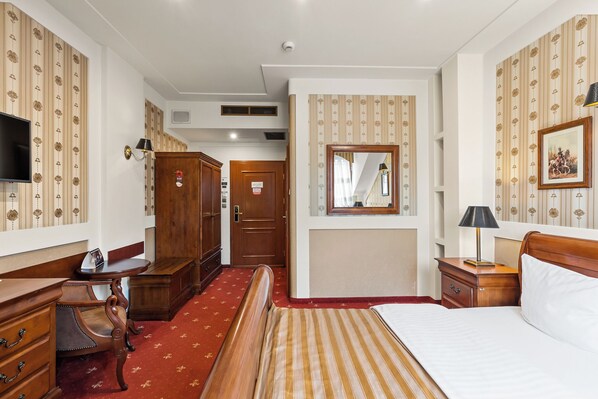 A hotel room with a bed, wooden furniture, a television, a wardrobe, and a mirror.