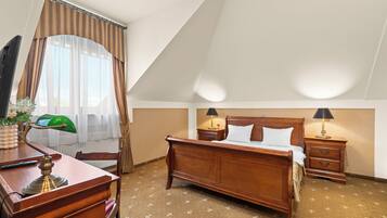 A hotel room with a wooden bed, two bedside tables with lamps, a desk with a lamp, a chair, and a window with curtains.